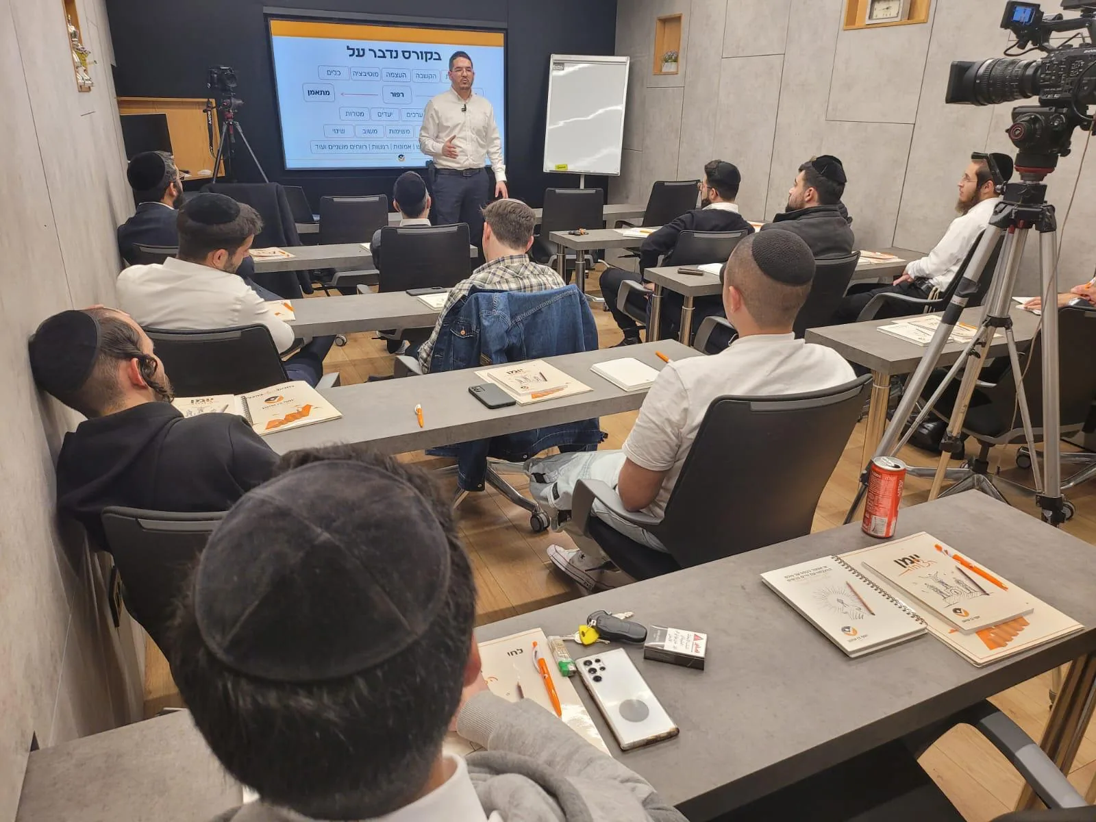 יוסף בן שושן מלמד קבוצת משתתפים בכיתה, מול מסך עם נושאי הקורס