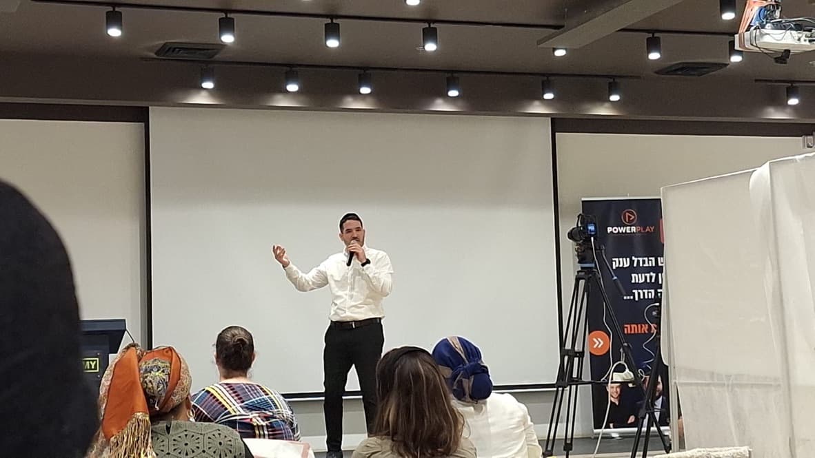 יוסף בן שושן על הבמה מול קהל, באולם הרצאות